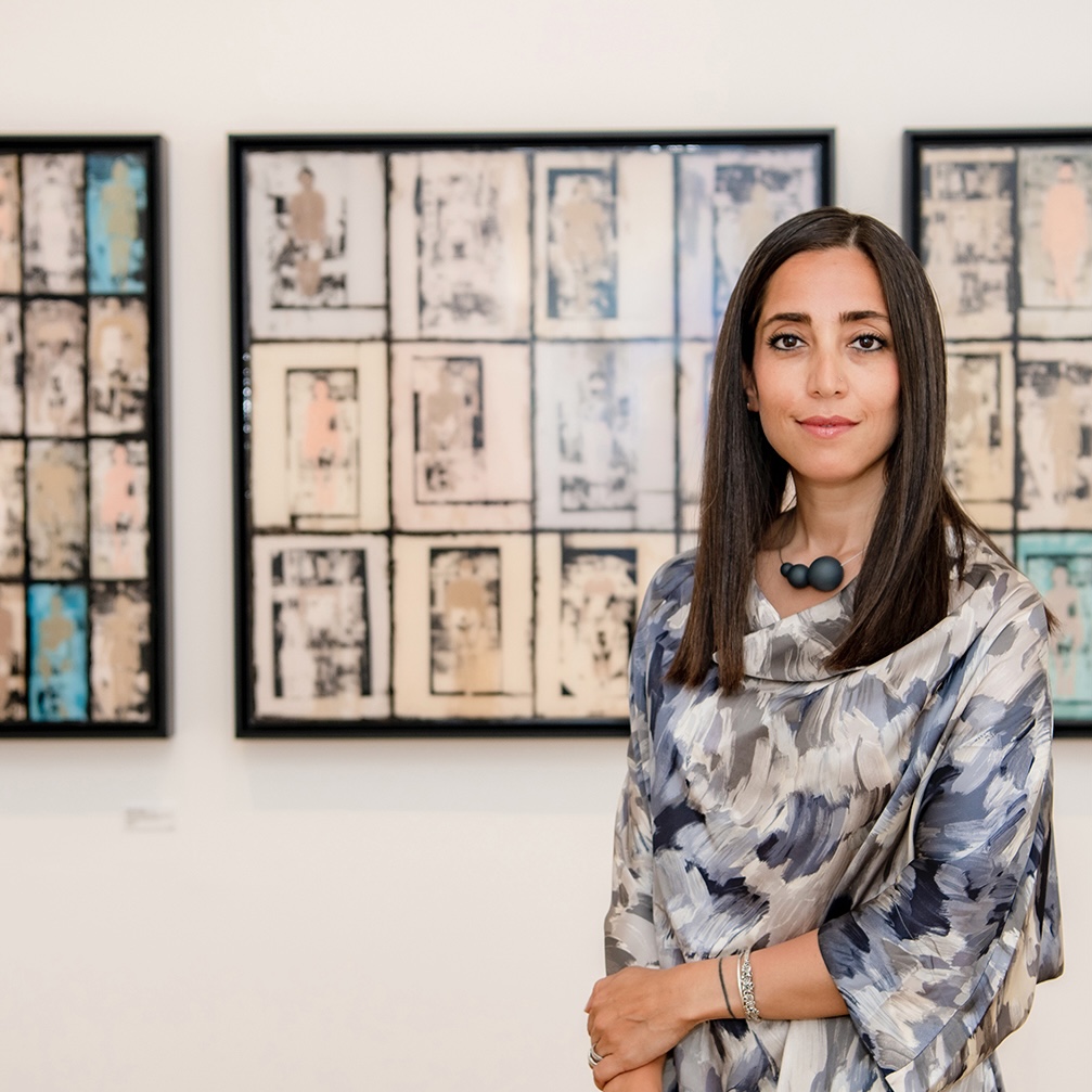 Portrait of Shadi Yousefian from waist-up, standing in front of three framed original prints