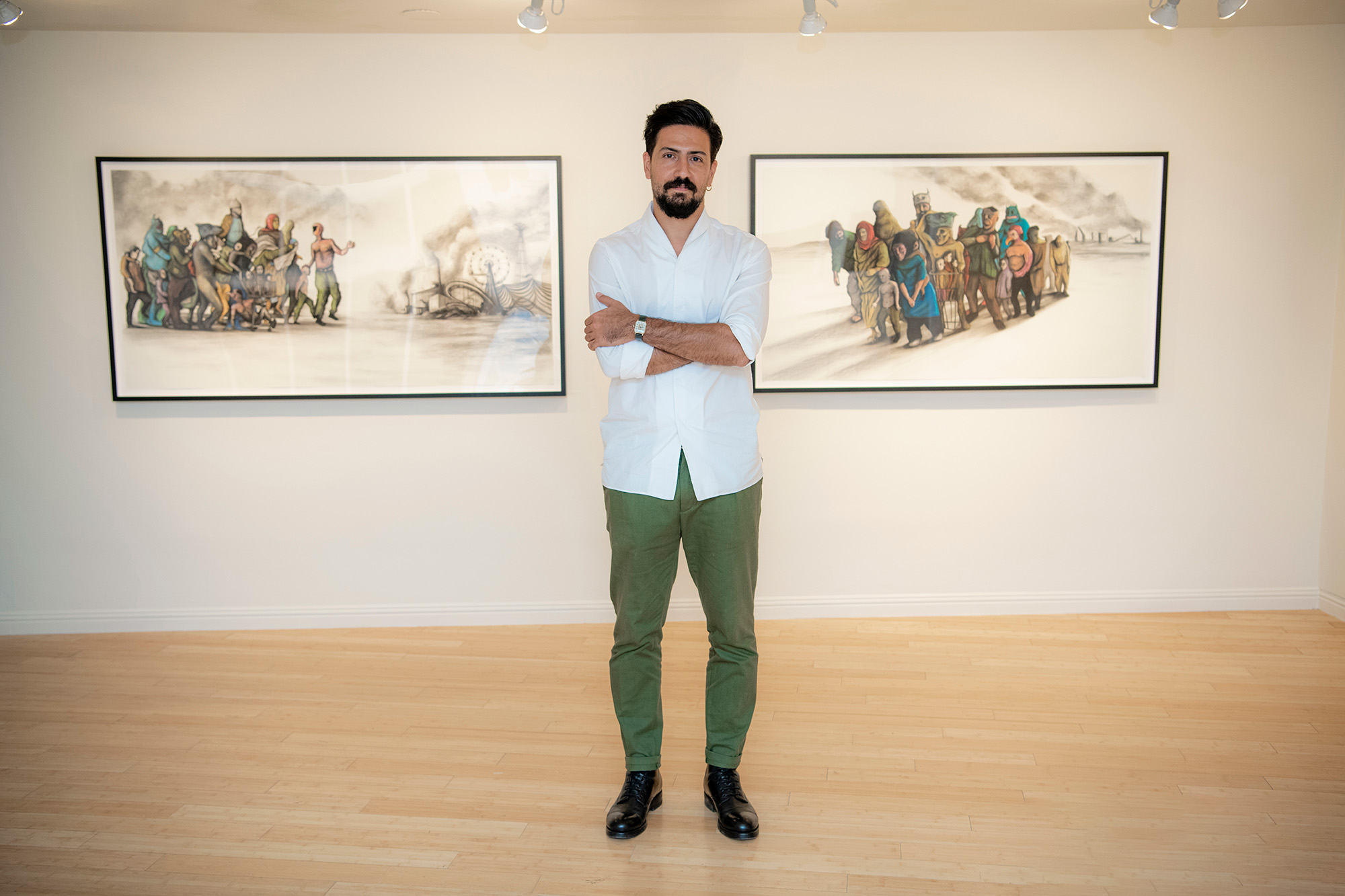 Portrait of Pouya Afshar standing in between two framed prints of digital paintings